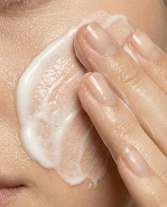 Dedos a espalhar creme suavemente na face