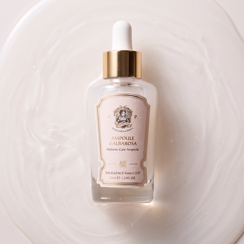 A clear glass dropper bottle of CDP Excellence from CDP Ampoule de Albarosa, featuring a white label with gold borders and a gold collar, resting on a white liquid surface with ripples.