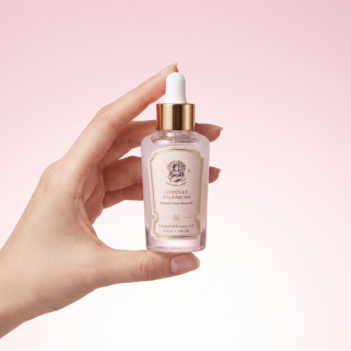 A hand holding a small glass dropper bottle of Ampoule Palmetta skin serum against a soft pink gradient background.