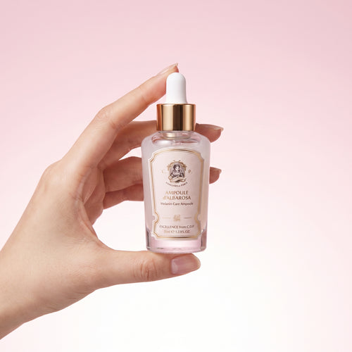 A hand holding a small glass dropper bottle of Ampoule Palmetta skin serum against a soft pink gradient background.