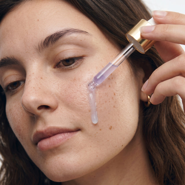 Pipeta de tampa dourada a aplicar sérum Memoria de tom lilás muito suave na face.